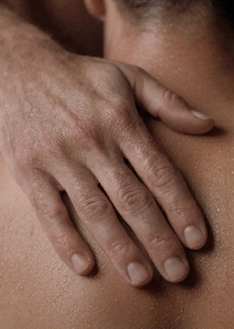 Ein Mann berührt einen anderen Mann aufmerksam in einer Tantra-Massage am Schulterblatt.