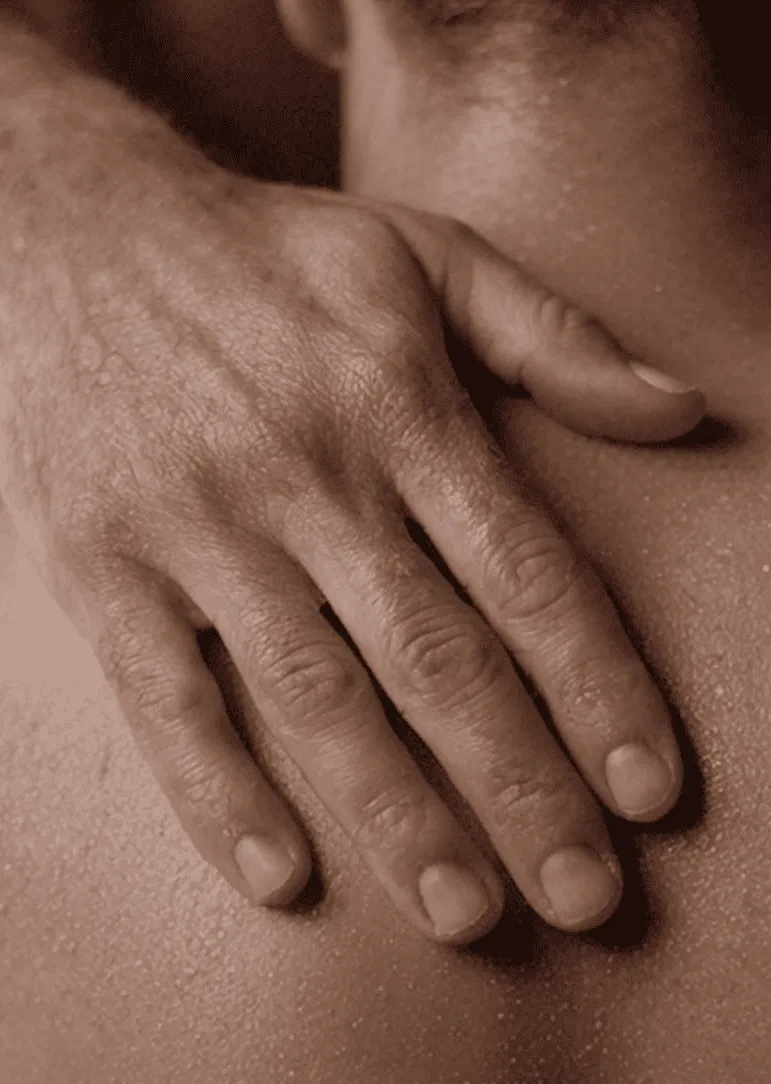 Ein Mann berührt einen anderen Mann aufmerksam in einer Tantra-Massage am Schulterblatt.